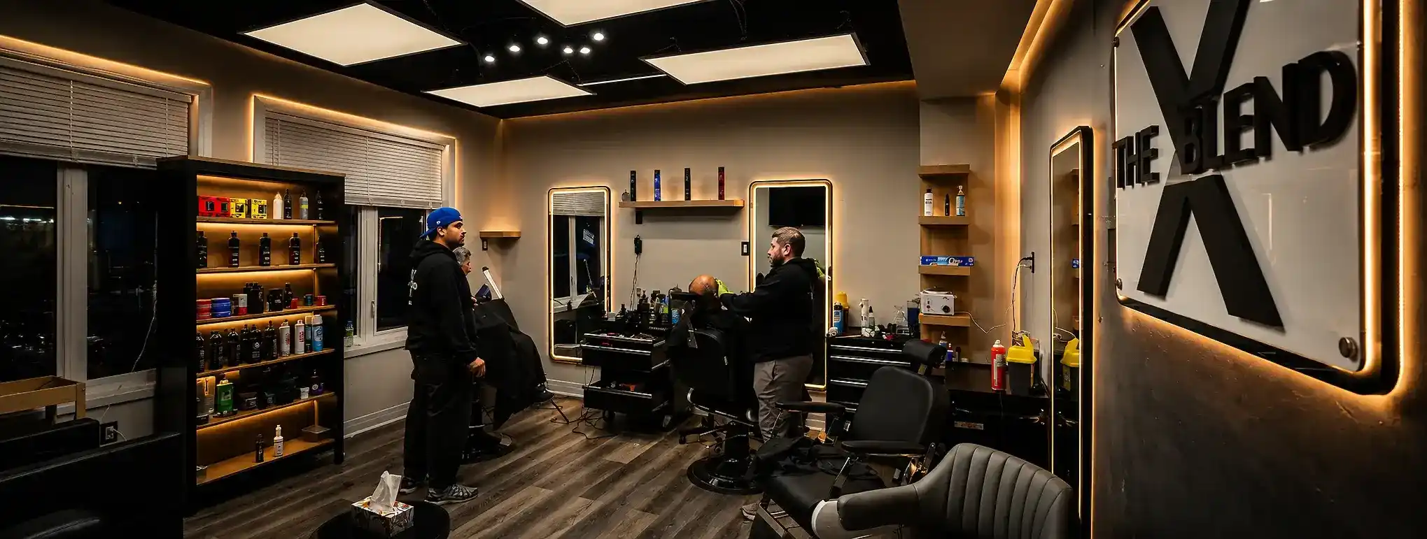 The X Blend barber shop interior featuring a professional barber giving a client a haircut in oakville, modern barber chairs, illuminated mirrors, and a stylish grooming salon atmosphere.