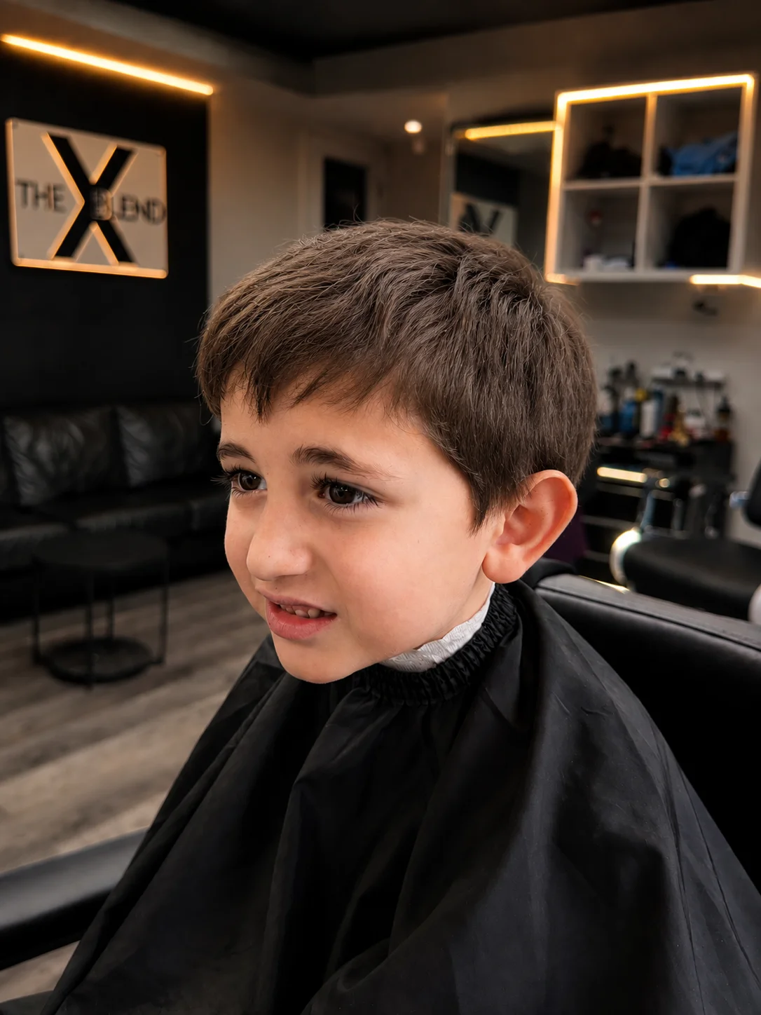 A young boy with natural, medium-length unstyled brown hair sitting in a barber chair.