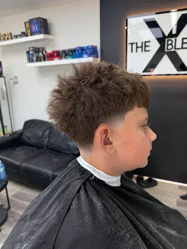 A young boy sits in the barber chair after receiving a fresh textured kids haircut with shorter sides and a fuller top in Oakville.