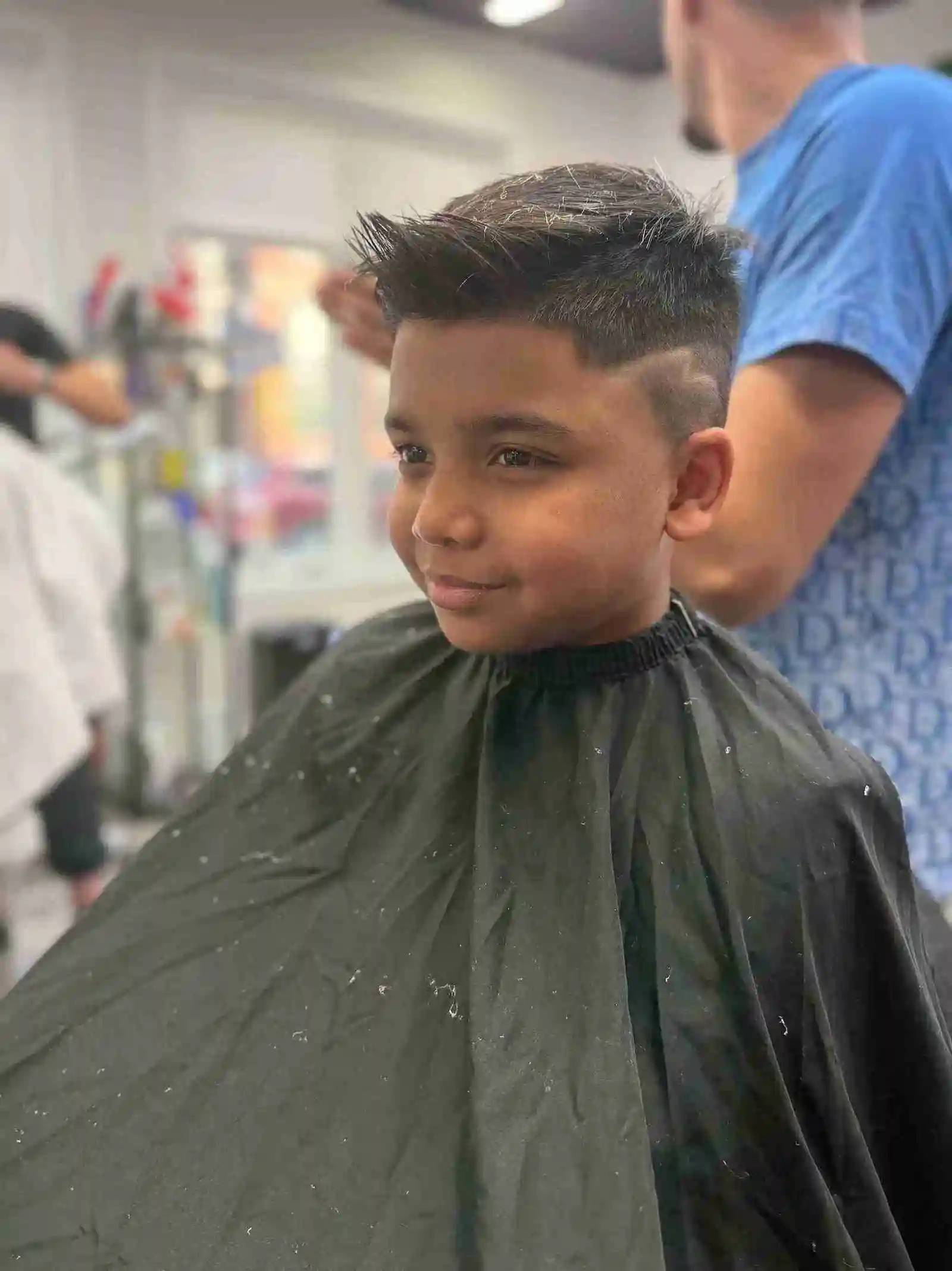 Young boy with a spiky short haircut and custom shaved side design sitting in an Oakville barber chair